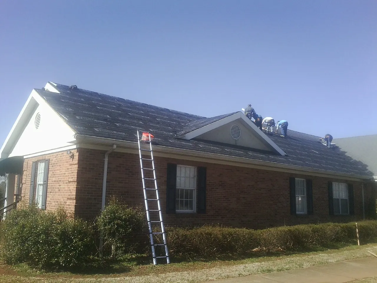 Crew tearing shingles off a brick ranch roof with a ladder set — Emergency Roof Repair work by our crew in Eglin Afb