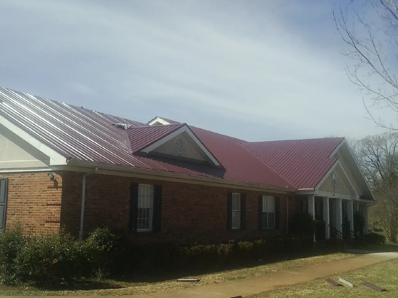 Red metal roof with gabled entries on a long brick building, from a Hail Damage Roof Repair job in Eglin Afb