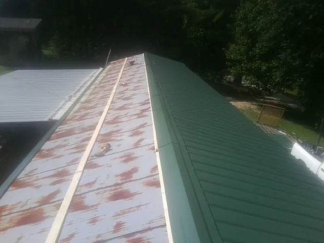 Old rusted panels beside newly installed green metal roofing — Wind Damage Roof Repair by Roofing Brothers in Eglin Afb