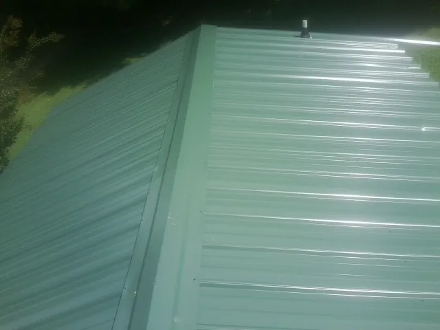 New green metal panels meeting at the ridge of a roof — Flat Roof Repair work by our crew in Eglin Afb