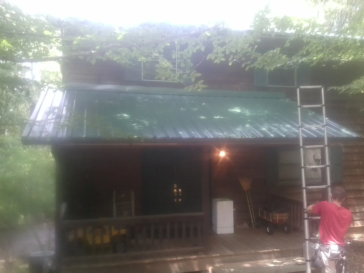 Worker on a ladder at the green porch roof of a wooded cabin in Eglin Afb