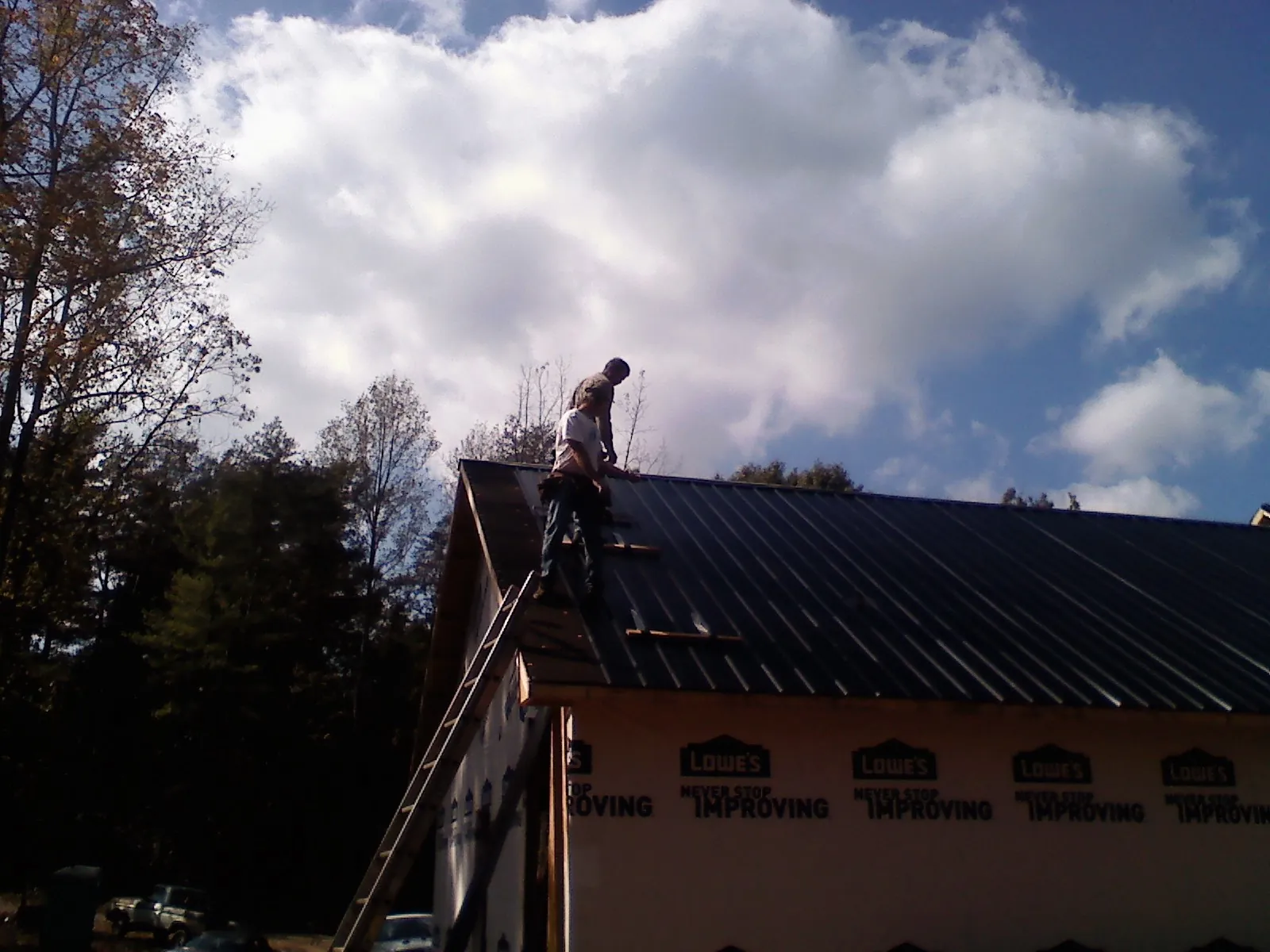 Roofer fastening dark metal panels high against a cloudy sky, from a Roof Inspection job in Eglin Afb